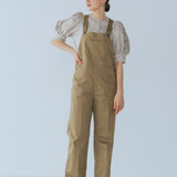 Camel-colored chino stretch overalls modeled on person, featuring large front patch pocket and adjustable shoulder straps for customizable fit