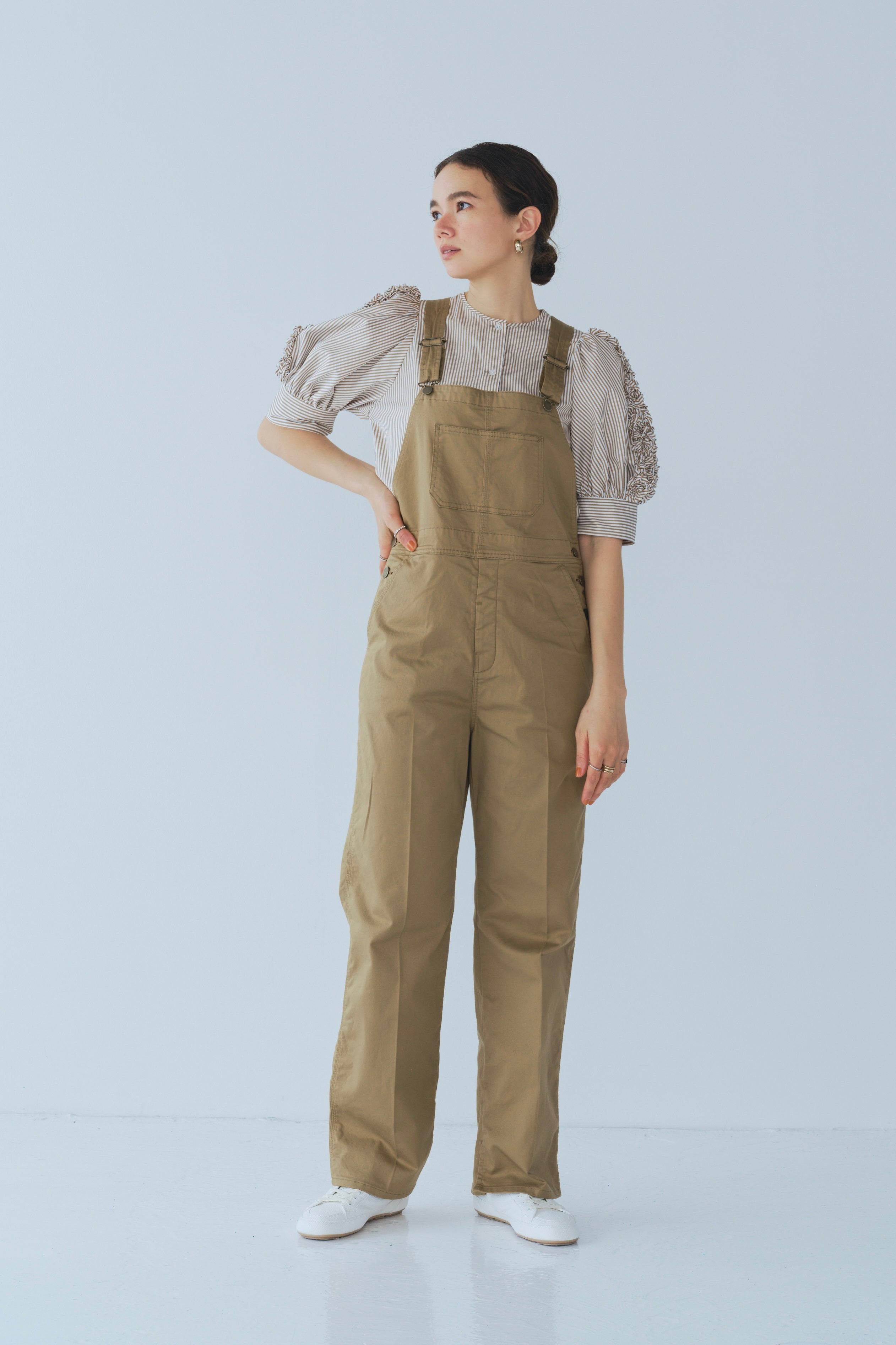 Camel-colored chino stretch overalls modeled on person, featuring large front patch pocket and adjustable shoulder straps for customizable fit